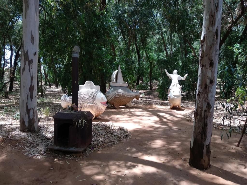 Ein Baumweg, gesäumt von Bäumen, weißen Statuen und einer kleinen Struktur.