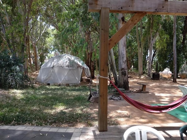 Un hamac sous une structure en bois, un espace salon abrité et une tente dans un cadre boisé.
