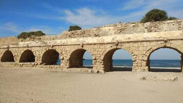 Una struttura in pietra con più archi, uno sfondo sabbioso e un cielo sereno.