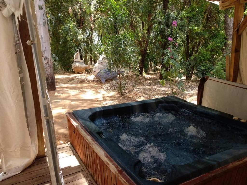 A hot tub in a wooded area with a wooden deck and a stone sculpture in the background.