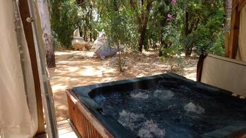 A hot tub in a wooded area with a wooden deck and a stone sculpture in the background.