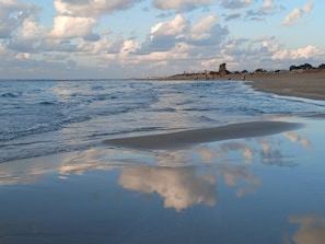 Ein Strand mit Wellen, einem klaren Himmel und einer fernen Felsformation.