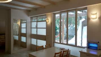 A room with a dining table, chairs, a heater, and large windows.