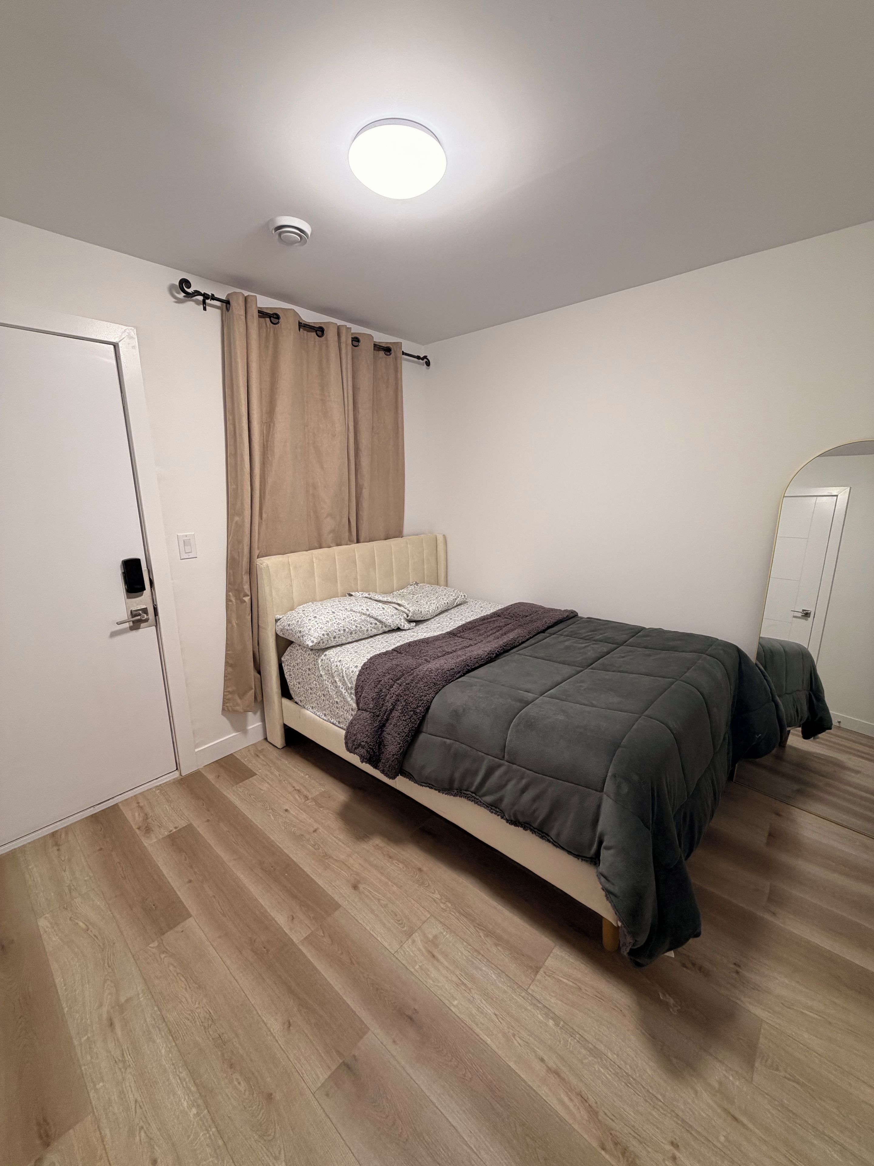 Un dormitori amb un llit, una porta, un mirall i una làmpada al sostre.