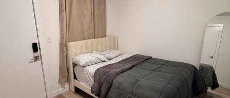 Un dormitori amb un llit, una porta, un mirall i una làmpada al sostre.