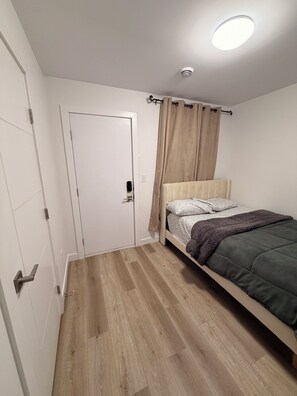 A bedroom with a bed, a door, a ceiling light, and a window with curtains. - Spacious well equipped bedroom and private washroom with a private entrance. (Winnipeg)