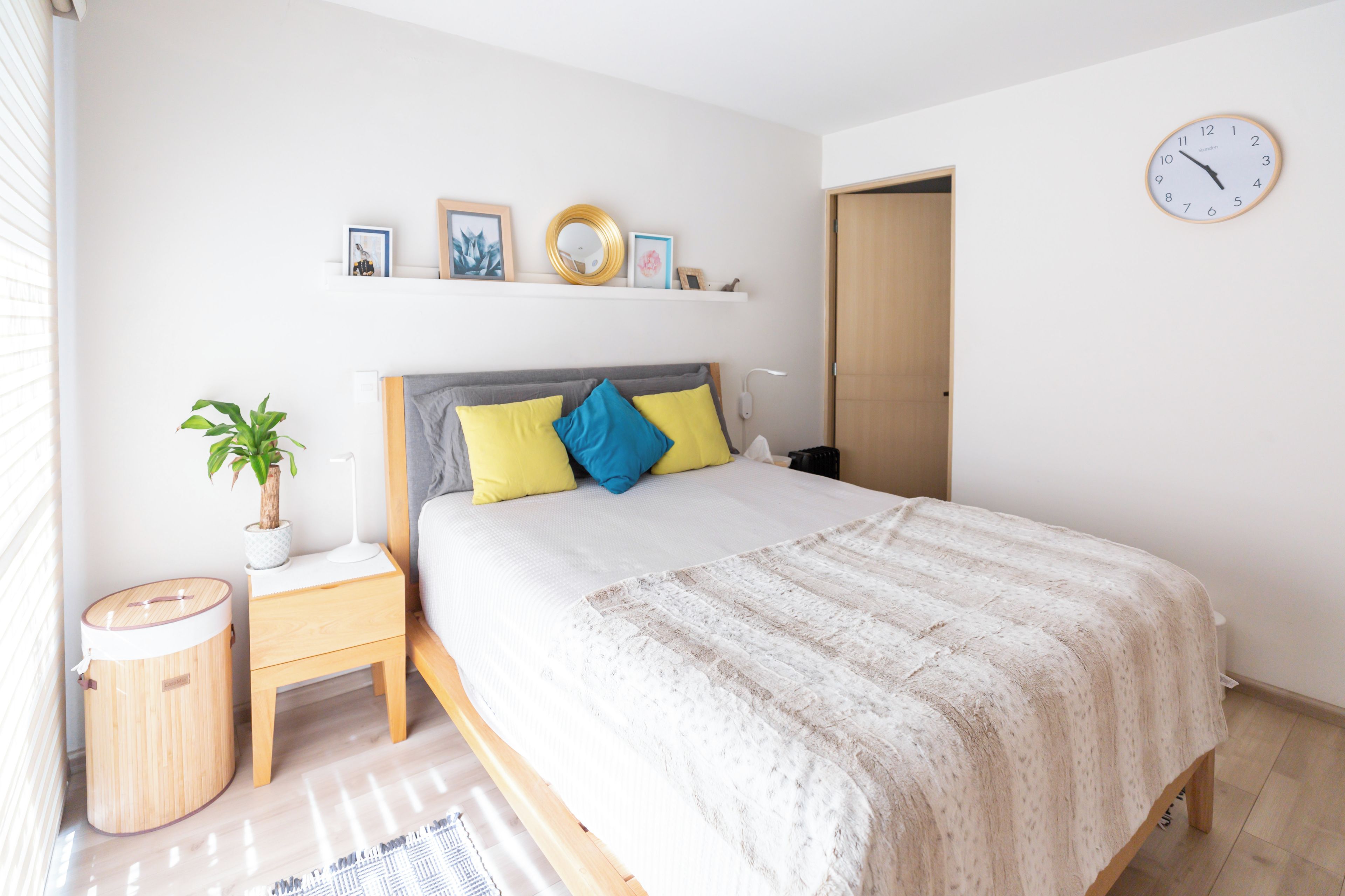 Un dormitorio con cama, mesitas de noche, un reloj de pared y una ventana con persianas.