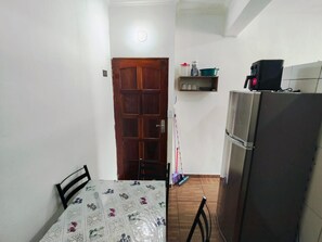 Cocina compacta con refrigerador, una puerta de madera y un estante con utensilios de cocina.