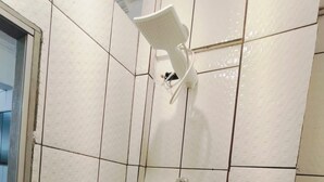 Kylpyhuone, jonka seinät on laatoitettu valkoisilla laatoilla, ja jossa on suihkupää sekä wc-istuin.