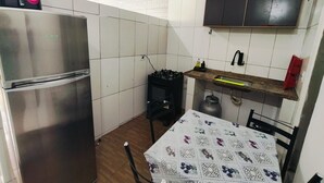 Kompakti keittiö, jossa on ruostumattomasta teräksestä valmistettu jääkaappi, kaasuliesi ja kuviollinen pöytäliina.