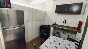Een compacte keuken met een roestvrijstalen koelkast, een gasfornuis en een tafel met een tafelkleed met een patroon.