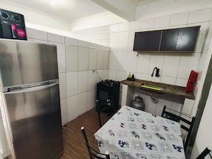 Una cocina compacta con un refrigerador de acero inoxidable, una estufa a gas y una mesa con mantel estampado.