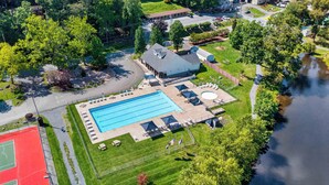 Ovenfra ses et boligområde med en swimmingpool, tennisbane og en mindre bygning med skråtag.