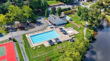 An aerial view of a residential area with a swimming pool, a tennis court, and a small building with a sloped roof.