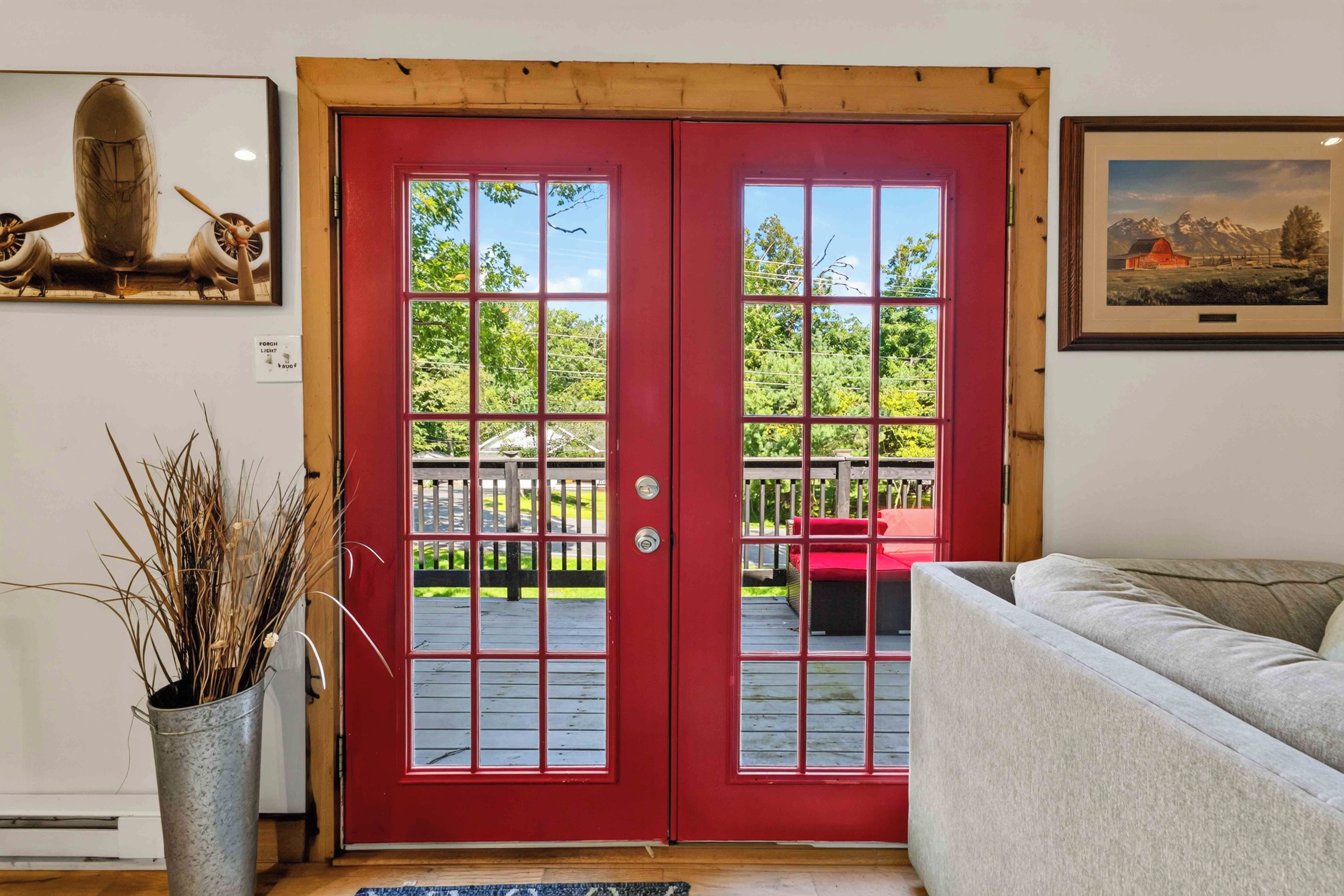 A red door with a view of a wooden deck and a white couch.