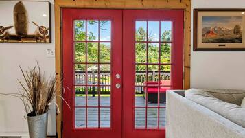 A red door with a view of a wooden deck and a white couch.