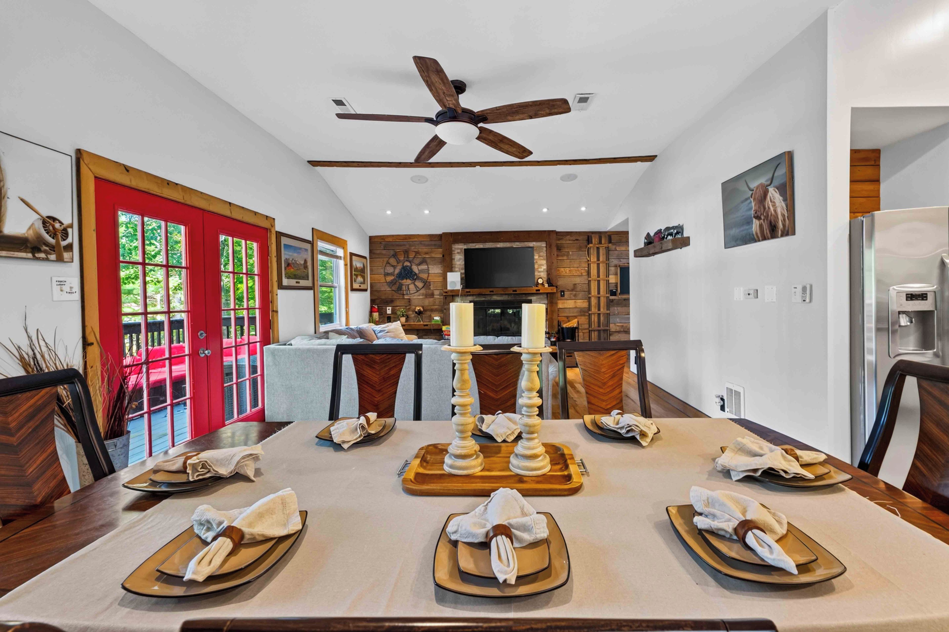 A dining area with a long table set for a meal, a ceiling fan, and a kitchen in the background.