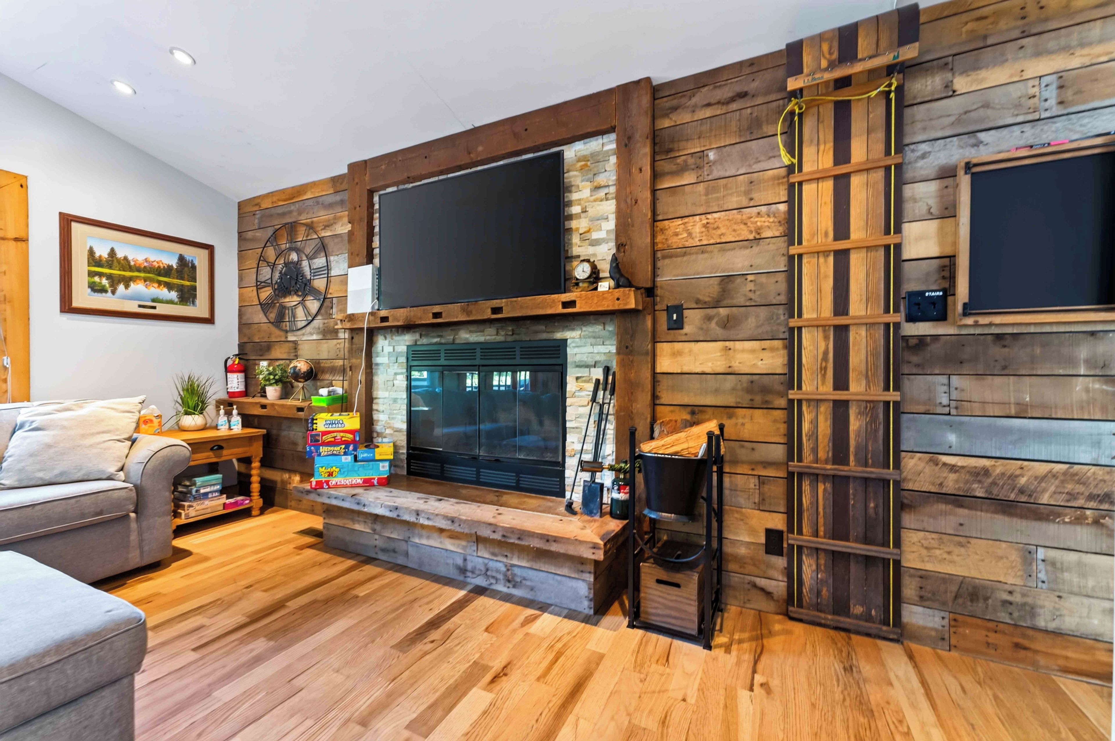 A living room with a fireplace, wooden wall paneling, a mounted clock, and a ladder.