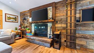A living room with a fireplace, wooden wall paneling, a mounted clock, and a ladder.