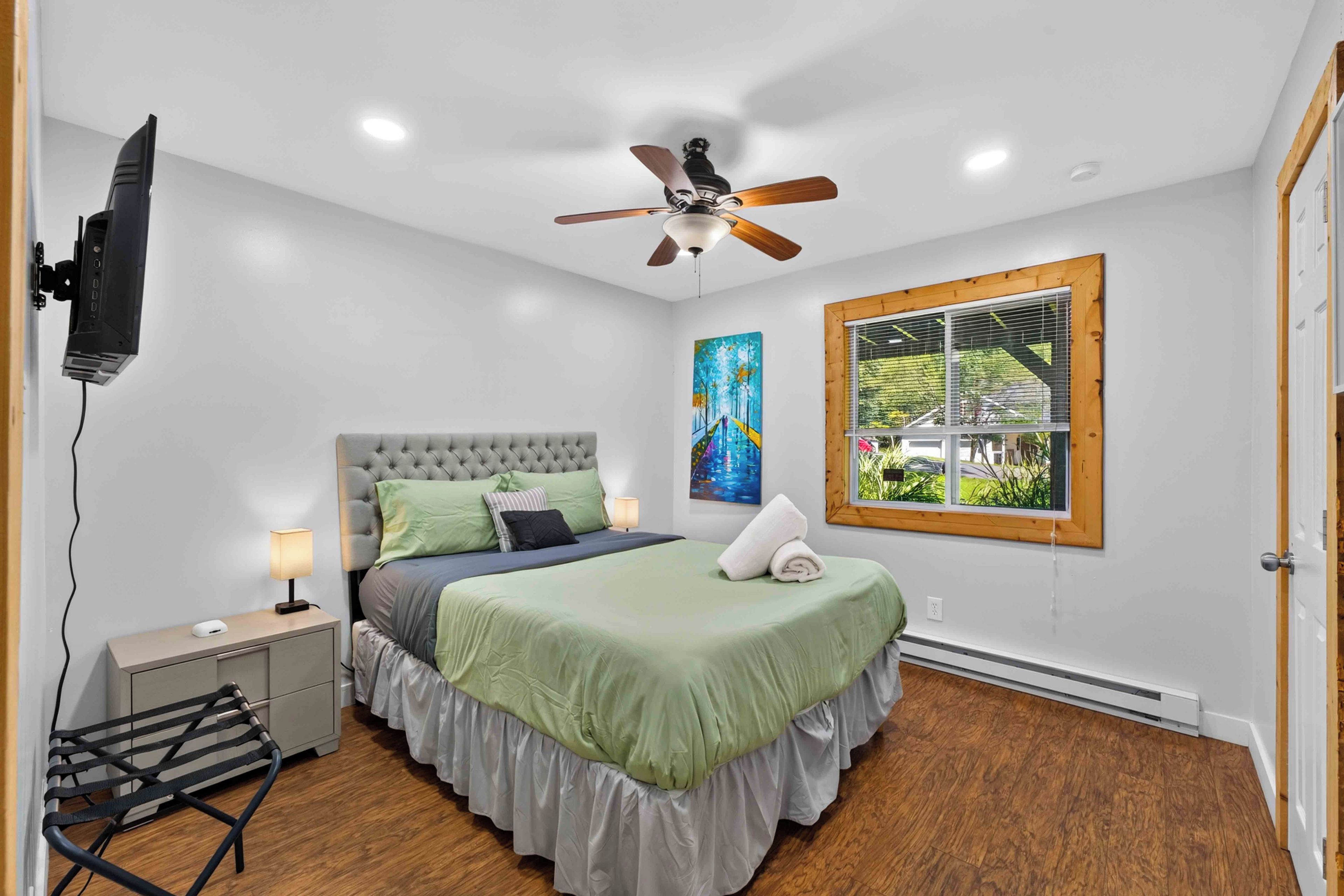 A bedroom with a bed, a ceiling fan, a window with blinds, and a painting on the wall.