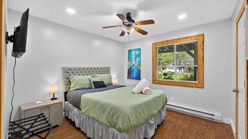 A bedroom with a bed, a ceiling fan, a window with blinds, and a painting on the wall.