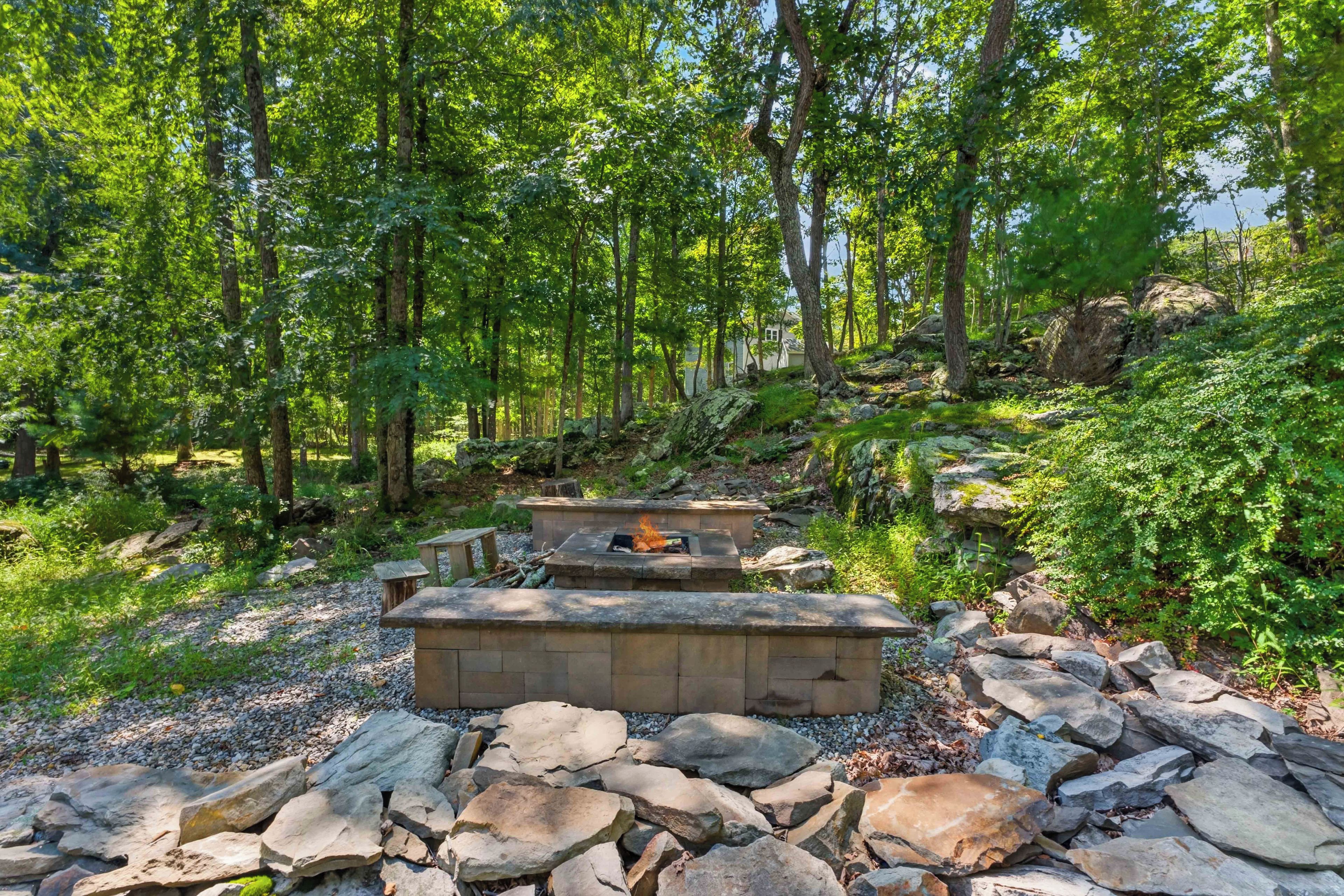 A forested area with a stone fire pit and seating area.