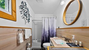 Et badeværelse med kommode i træ, vask, toilet, brusebad og et spejl.