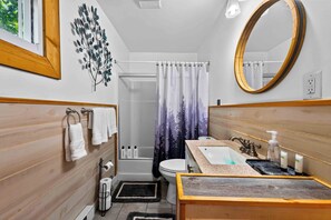 A bathroom with a wooden vanity, a sink, a toilet, a shower, and a mirror. - Saw Creek 4-Bed Mountain Escape w/fire pit (Saw Creek)