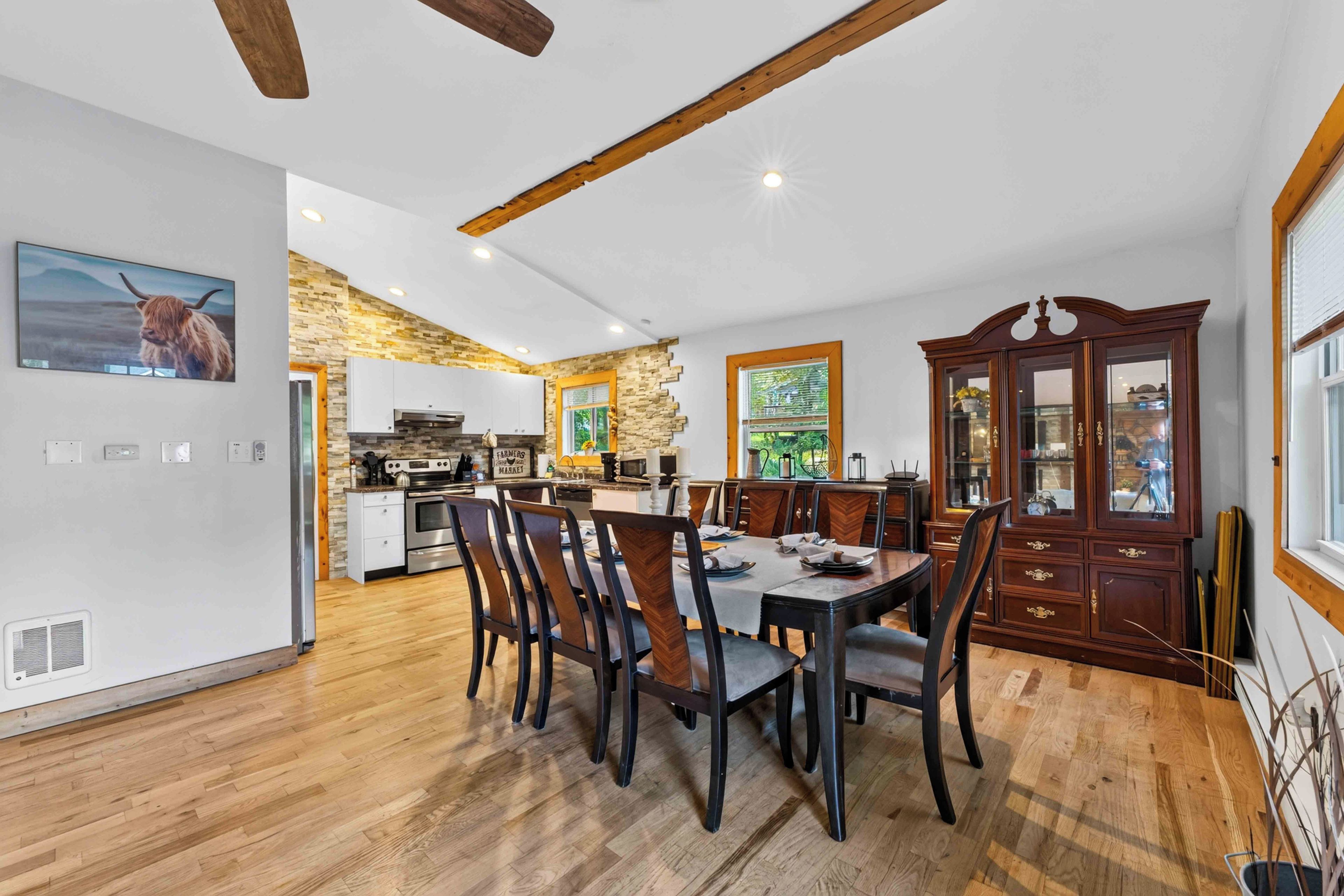 A spacious kitchen with modern appliances, a dining area with wooden chairs, and a large cabinet with glass doors.