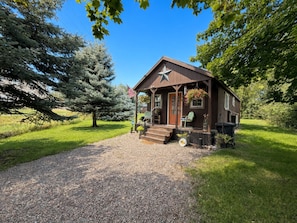 A rustic cabin with a porch, a star decoration, and a gravel driveway. - Cozy Cabin Glacier Getaway - Fireplace & Firepits (Kalispell)