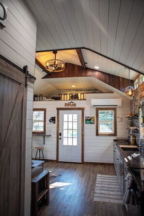 A rustic interior with a wooden ceiling, a kitchen area with a sink and countertop, and a door with a window. - Cozy Cabin Glacier Getaway - Fireplace & Firepits (Kalispell)