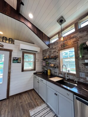 A kitchen with a rustic design, featuring a brick wall, wooden beams, and a large window. - Cozy Cabin Glacier Getaway - Fireplace & Firepits (Kalispell)