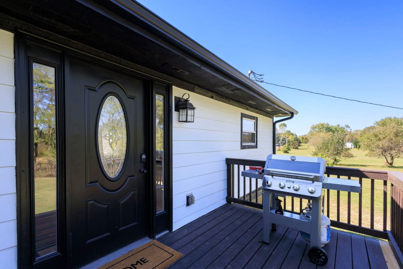 A house with a black front door, a grill on the deck, and a clear view of the surrounding landscape.