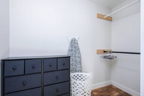 A room with a dark-colored dresser, a white laundry basket, and a wooden shelf. - Family-Friendly 4BR Home with Acreage in Addison (Addison)