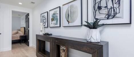 Un couloir avec une console en bois foncé, une plante en pot et une œuvre d’art abstrait accrochée au mur.