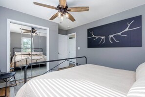 Quarto com cama, ventilador de teto, uma obra de arte na parede e escada para outro cômodo.