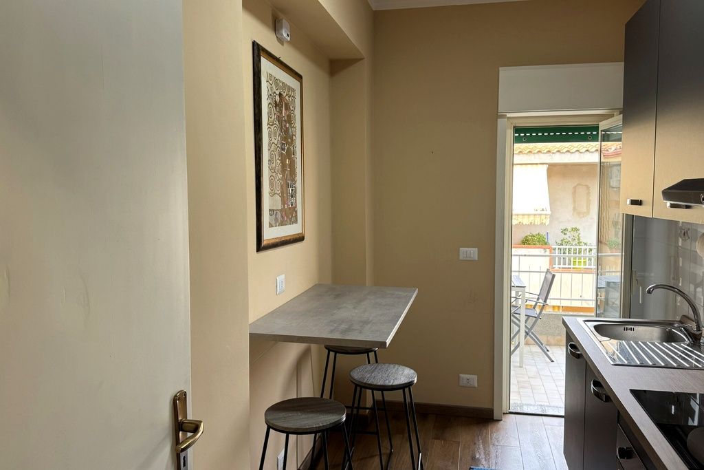 Een gezellige keuken met een eettafel en krukken, een hangend kunstwerk en uitzicht op een balkon.
