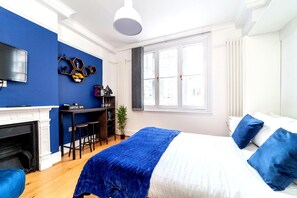 Un dormitorio con chimenea, una cama con ropa de cama azul, una barra de café y un ventanal grande.