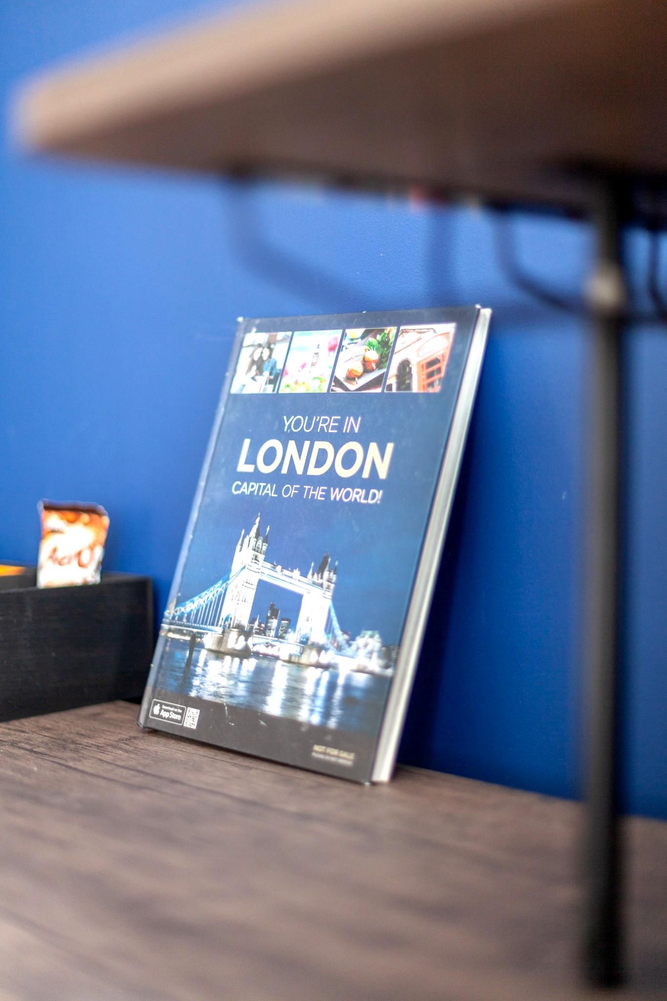 A book titled 'You're in London' on a wooden surface with a blue wall in the background.