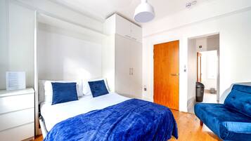A bedroom with a bed, a wardrobe, a wooden door, a blue chair, and a white ceiling light.