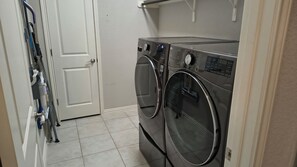 A laundry room with two stacked front-loading washing machines, a door, and a tiled floor. - Serene 3-bedroom house. Less than 5 minutes to restaurants and entertainment. (Georgetown)