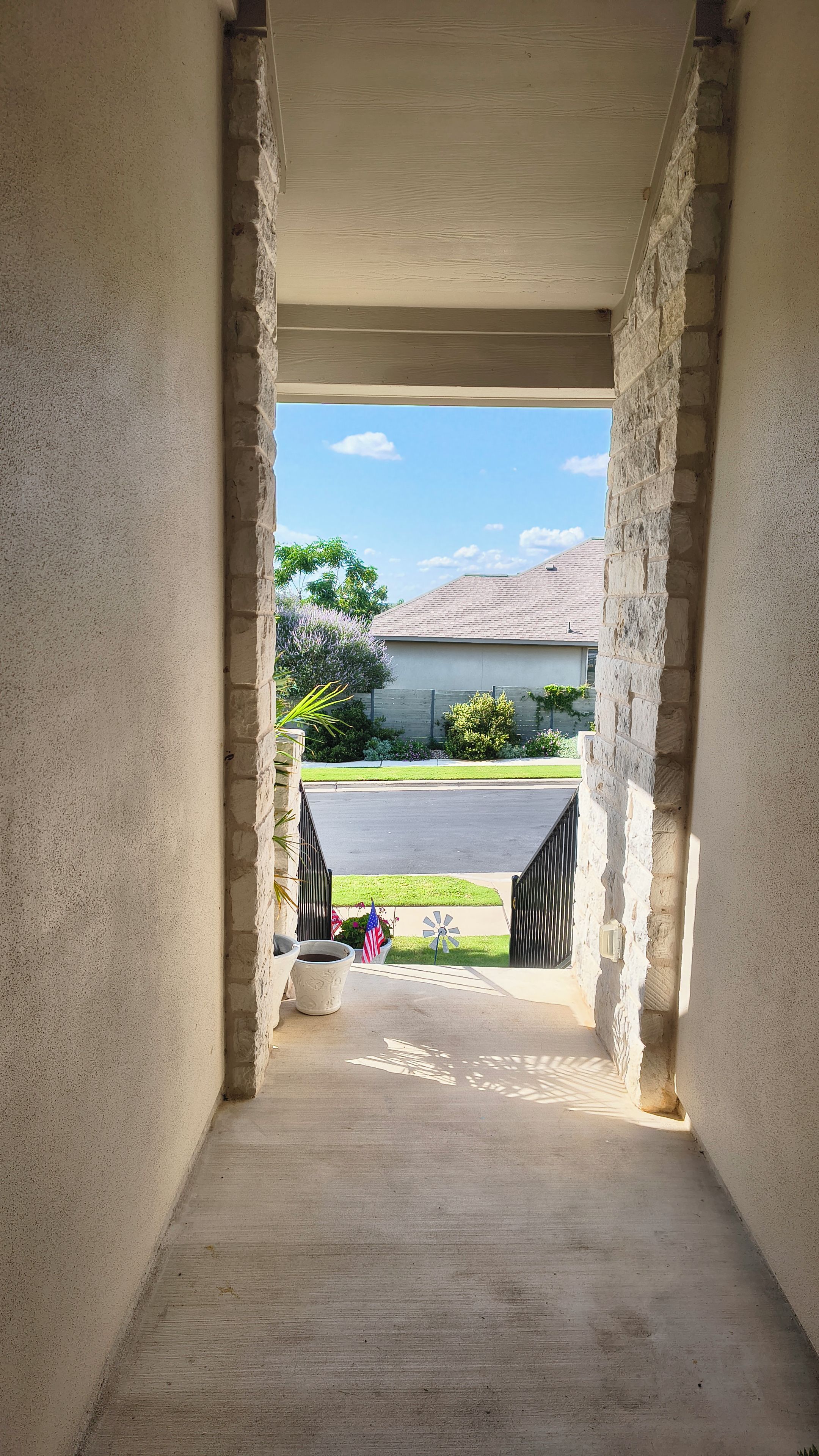 A concrete corridor with a view of a residential area, including a house and a lawn.