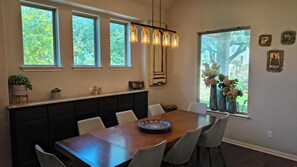 A dining area with a wooden table, white chairs, a chandelier, and a window with a view of greenery. - Serene 3-bedroom house. Less than 5 minutes to restaurants and entertainment. (Georgetown)