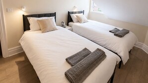 A bedroom with two beds, each with a headboard, a nightstand, and a lamp.