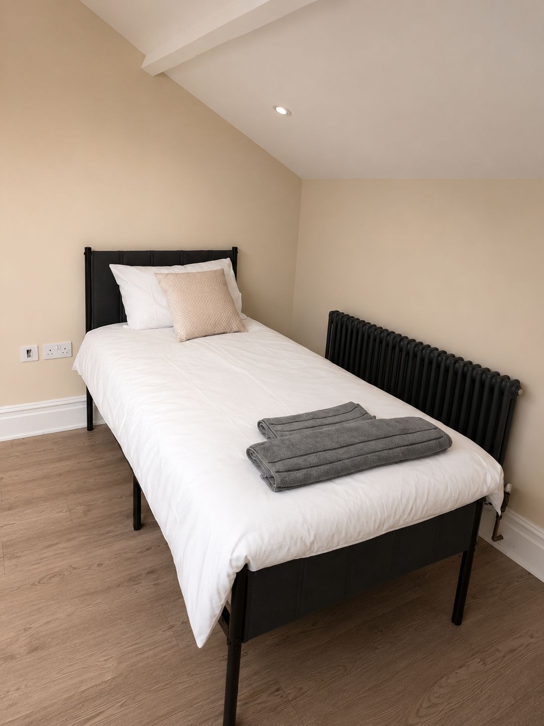 Een slaapkamer met een bed, een radiator en een houten vloer.