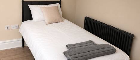Een slaapkamer met een bed, een radiator en een houten vloer.