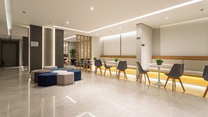 Een moderne lobby met een receptiebalie, een zithoek en een trap.