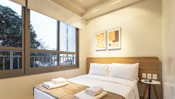 Een hotelkamer met een groot raam, een bed met witte lakens en twee ingelijste kunstwerken aan de muur.