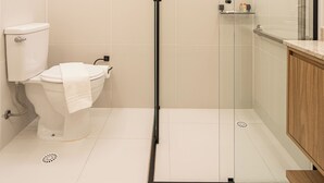 Een moderne badkamer met een douche met glazen wand, een toilet en een houten wastafelmeubel.