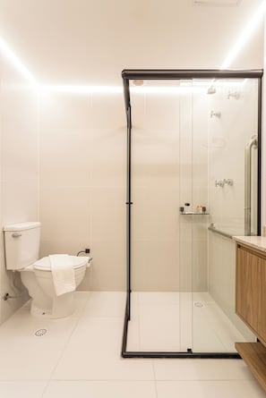 A modern bathroom with a glass-enclosed shower, a toilet, and a wooden vanity. - Lisboa by Bhomy (São Paulo)
